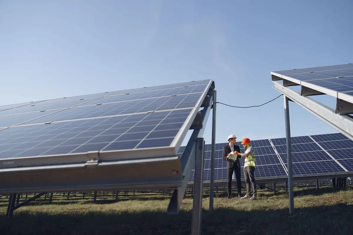 Trabajador con chaleco y casco de seguridad de pie entre paneles solares en un techo