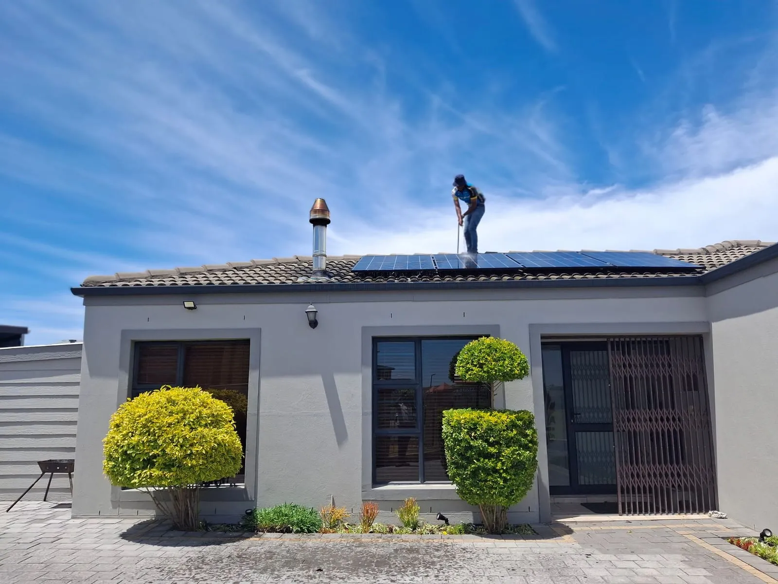 Técnico instalando paneles solares en el techo de una casa bajo cielo despejado